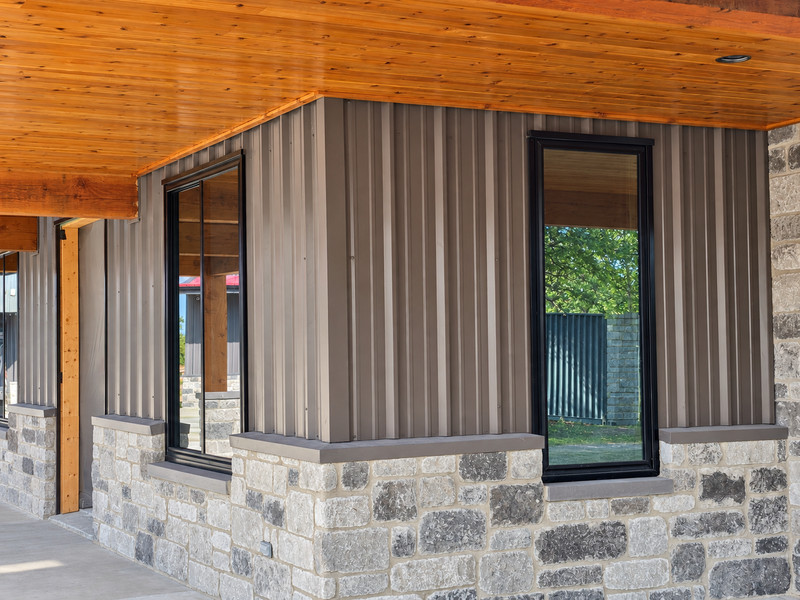 Dark-framed windows beneath a wood porch ceiling in a metal-and-stone exterior.