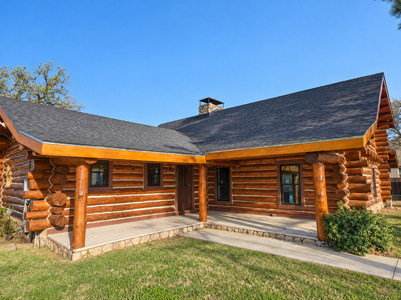 A log home with dark-framed windows beside a covered porch and a curved path.