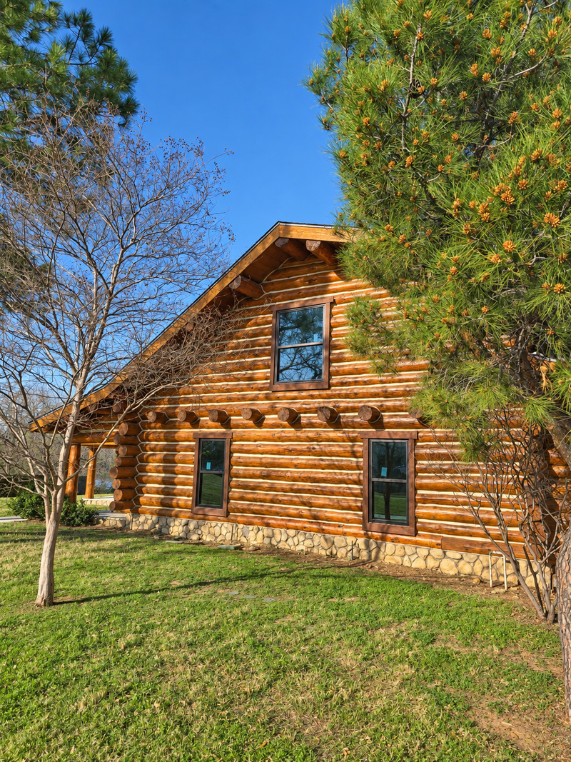 Three dark-framed windows with horizontal divisions in a log-home gable beneath trees.
