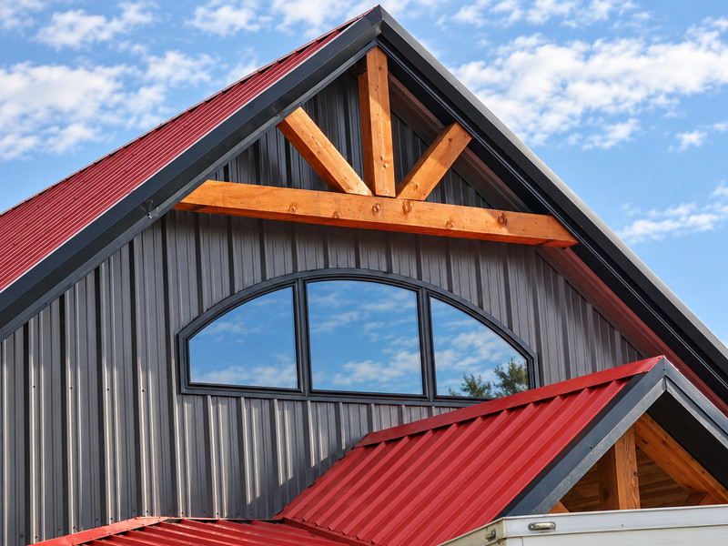 A three-section arched window below a timber-framed gable and red metal roof.
