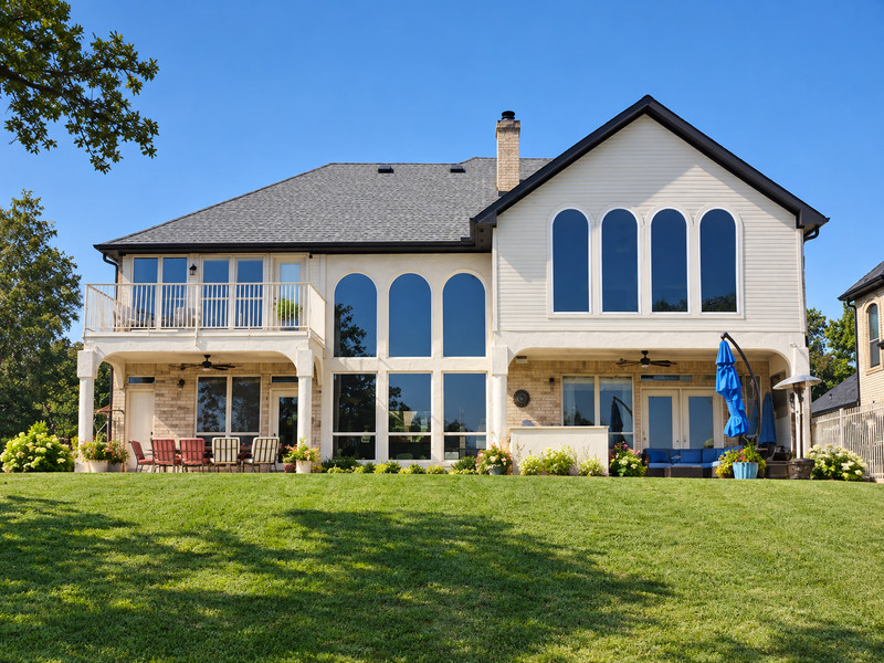 A white two-story home with seven tall arched upper windows overlooking a lawn.