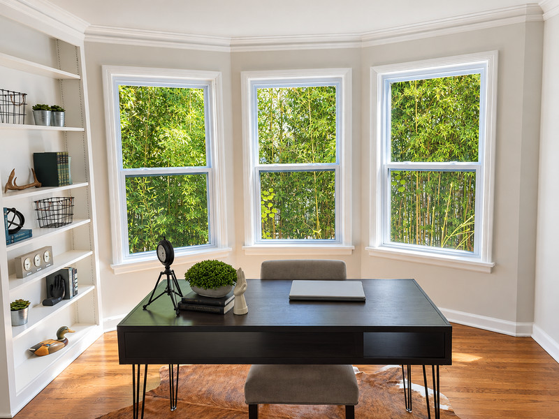Three white-framed windows with horizontal sash divisions around a desk beside built-in shelves.