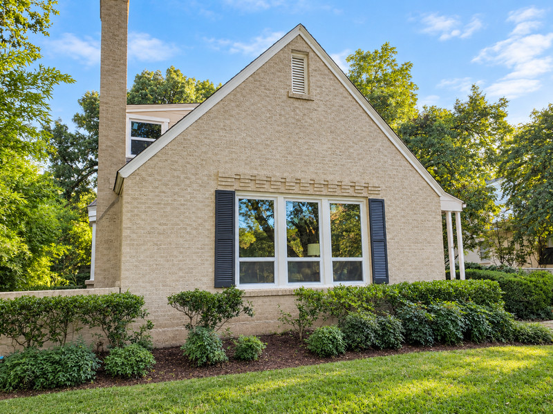 Three white-framed windows with low horizontal divisions and dark shutters beneath a brick gable.
